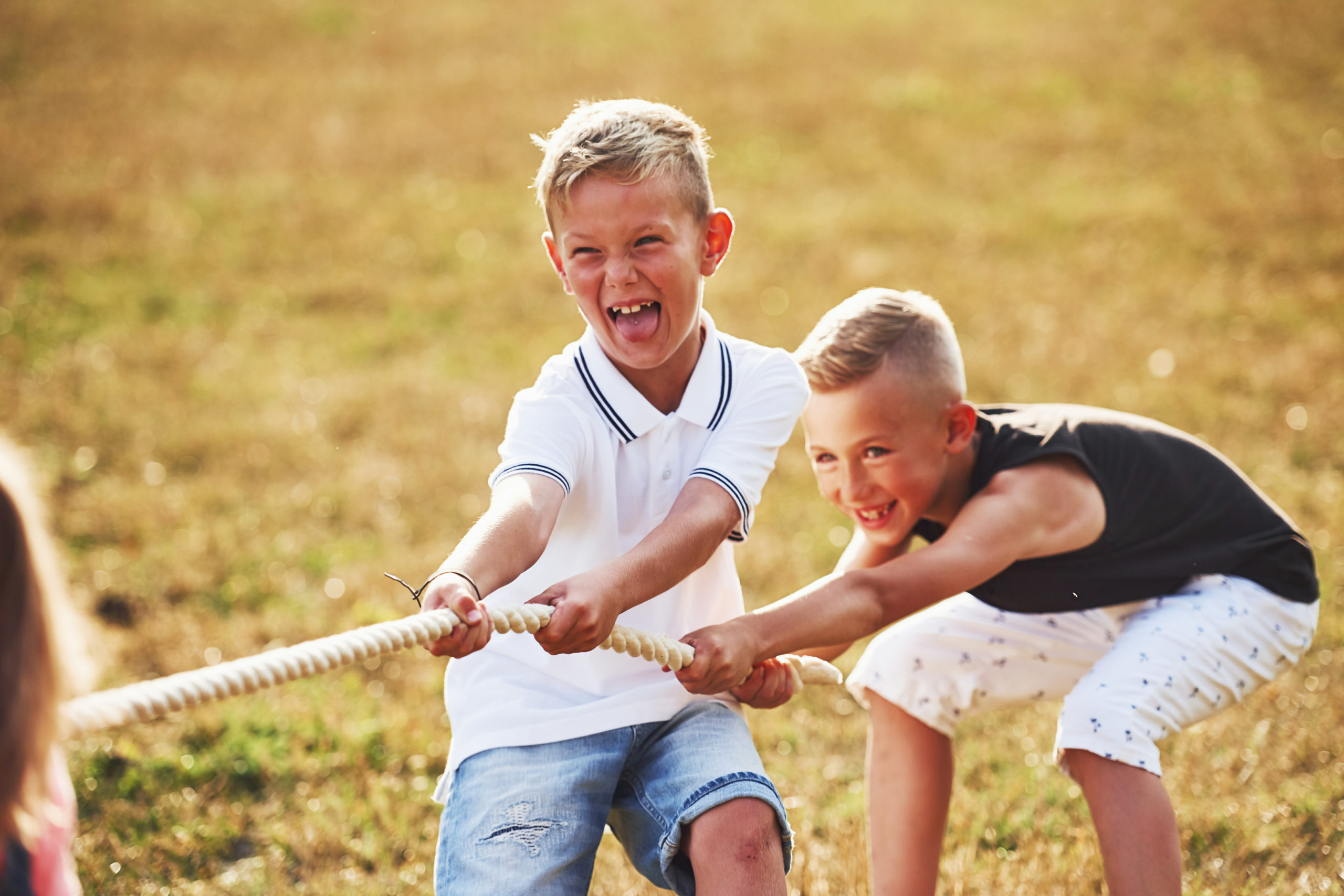 Kids playing tug of war game in the beautiful meadow at sunny day